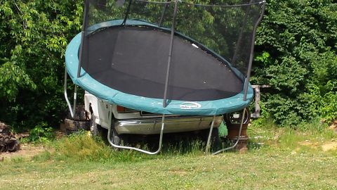 1979 Ford Bronco - A trampoline is precariously balanced on the front of a white truck.