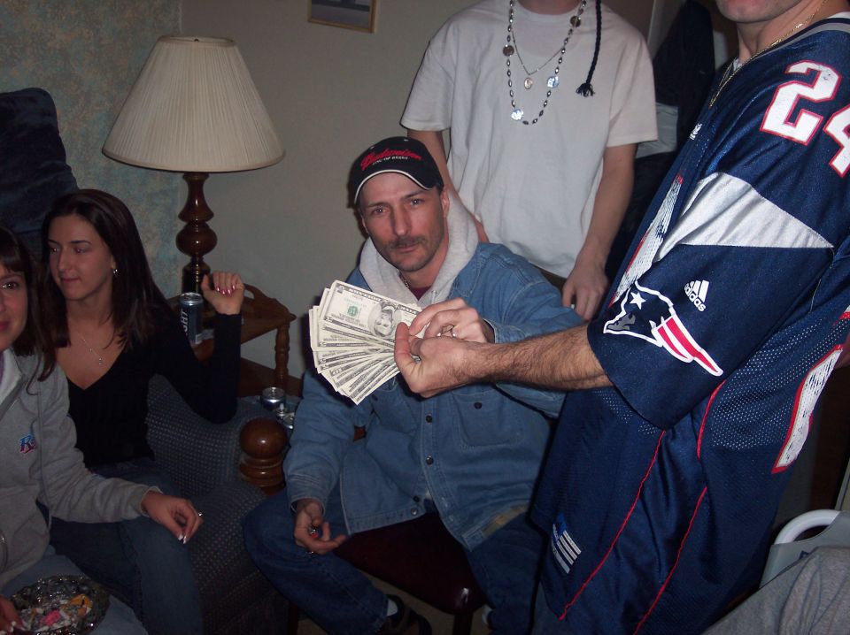 People gathered indoors, one man holds a fan of US dollar bills