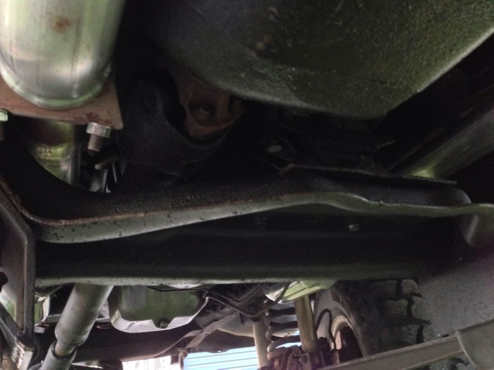 Underside view of a vehicle's frame, suspension, and exhaust system. A tire is visible on the right