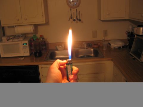 1995 Ford Bronco - A hand holds a lighter with a bright flame in front of a kitchen sink and microwave.