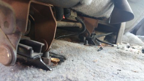 1995 Ford F-150 - Close-up view of the seat mounting hardware and wiring located beneath the carpet in a vehicle interior.