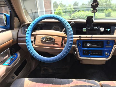 1994 Ford Crown Victoria - The interior of a 1994 Ford Crown Victoria features a blue steering wheel cover and a blue-trimmed center console with a radio.