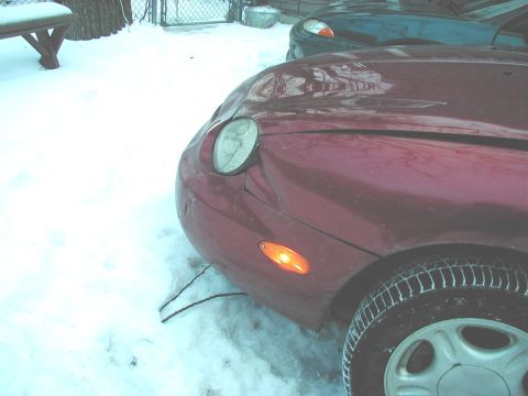 1997 Ford Taurus - A red 1997 Ford Taurus sits in the snow, its front fender and headlight visible, with another vehicle behind it.
