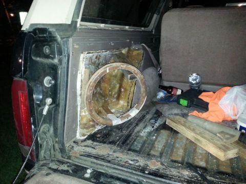 1996 Ford Bronco - The interior of a vehicle's cargo area is shown, with a circular opening in the side panel and items scattered on the floor.
