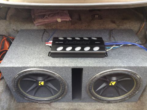 1994 Ford Crown Victoria - The trunk of a car contains a dual subwoofer enclosure and an amplifier, with wiring connected.
