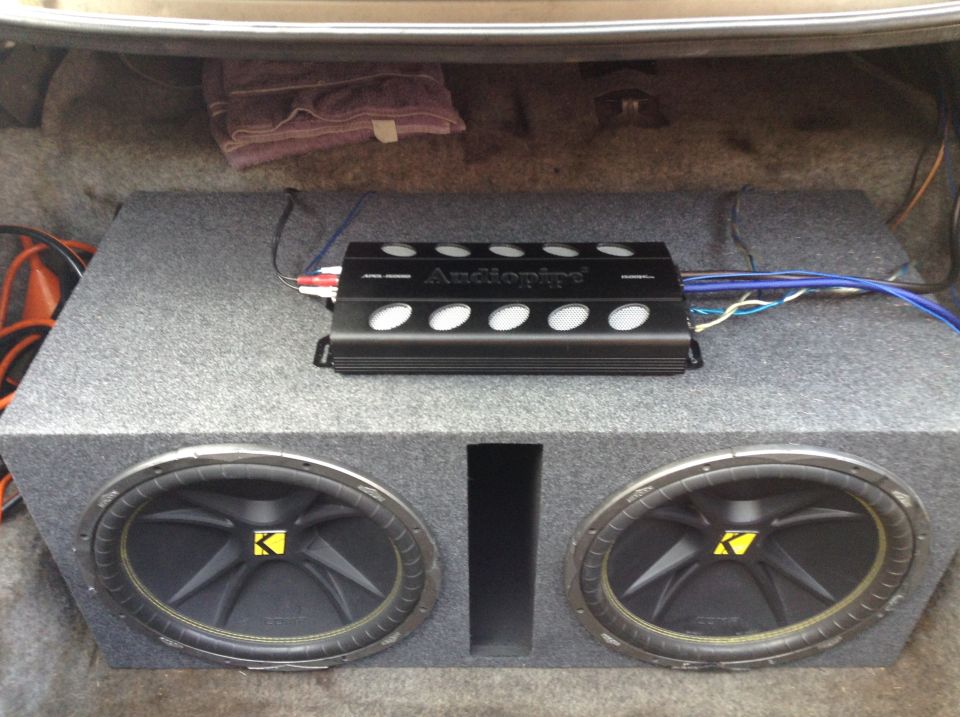 Car trunk interior with a dual Kicker subwoofer box and an Audiopipe amplifier. A folded towel is visible in the upper left