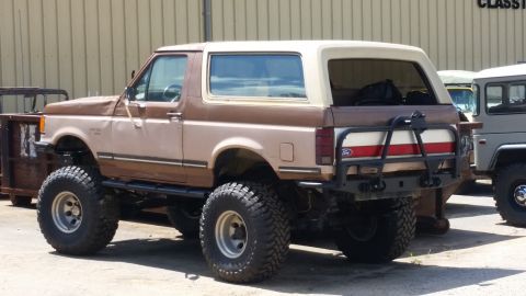 1988 Ford Bronco - This lifted two-tone brown SUV appears to be a 1987 Ford Bronco, modified with large off-road tires.