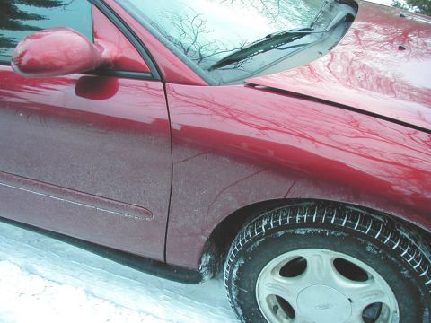 1997 Ford Taurus - A red 1997 Ford Taurus is partially visible in this close-up shot, showing its front fender and driver's side door.