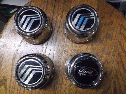 1999 Mercury Grand Marquis - Three Mercury hubcaps and one Ford hubcap are displayed on a wooden table.