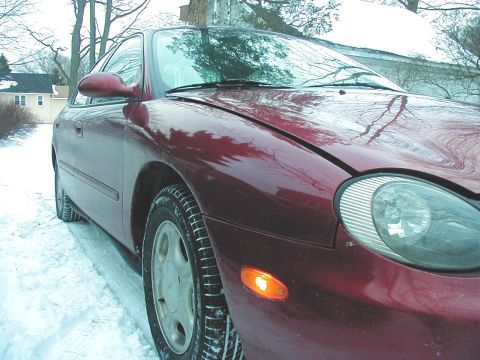 1997 Ford Taurus - A red 1997 Ford Taurus is parked on a snowy road, seen from the front three-quarter angle.