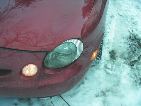1997 Ford Taurus - Close-up of a red car's front corner, showing the headlight and turn signal in snowy conditions.