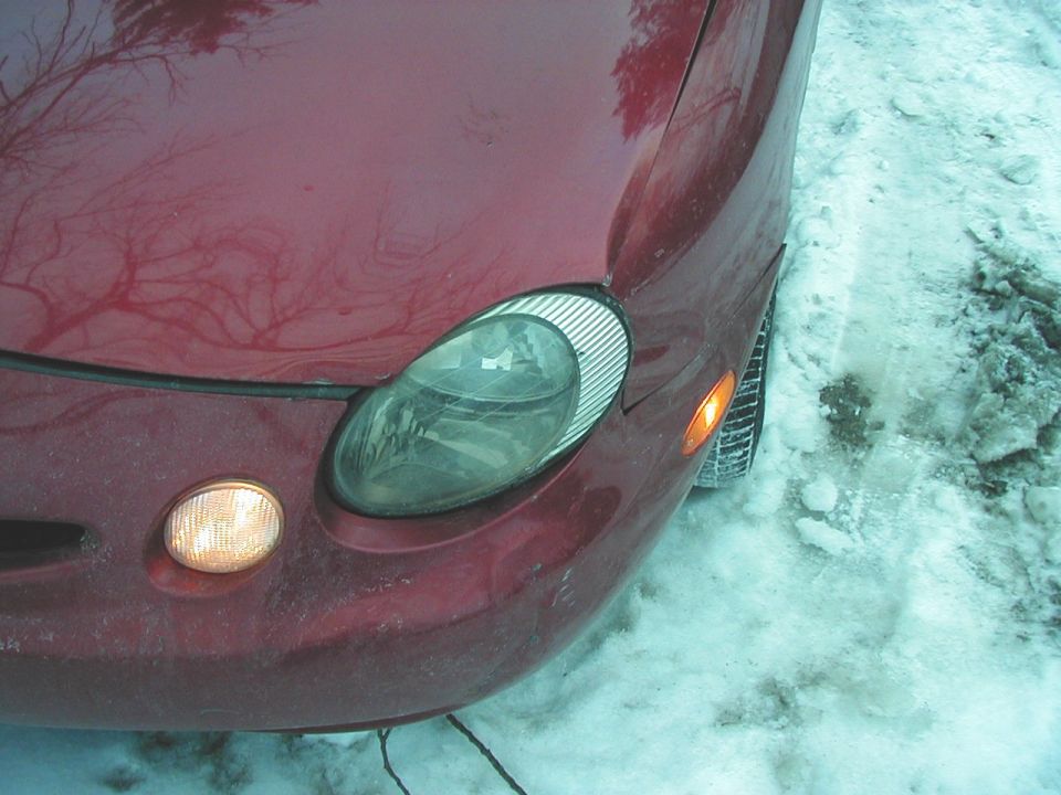 Red car's front fender and headlight assembly with amber turn signal light. Snow is on the ground