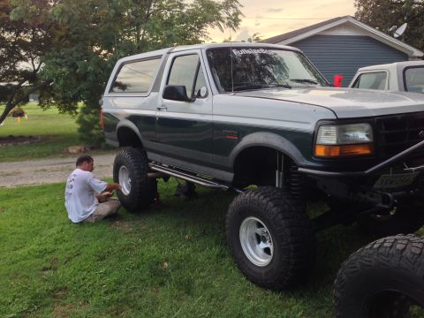 1979 Ford Bronco - A lifted 1996 Ford Bronco is parked on grass while a person works on its front wheel.