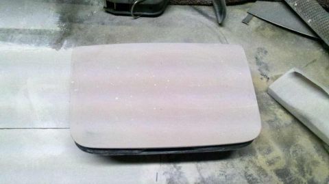 1982 Ford Bronco - A close-up view of a light-colored, rectangular object with rounded corners, possibly a car part, covered in a fine dust. The object is res…