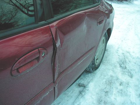 1997 Ford Taurus - The driver's side of a red sedan shows severe damage, with the rear door and quarter panel creased and misaligned.