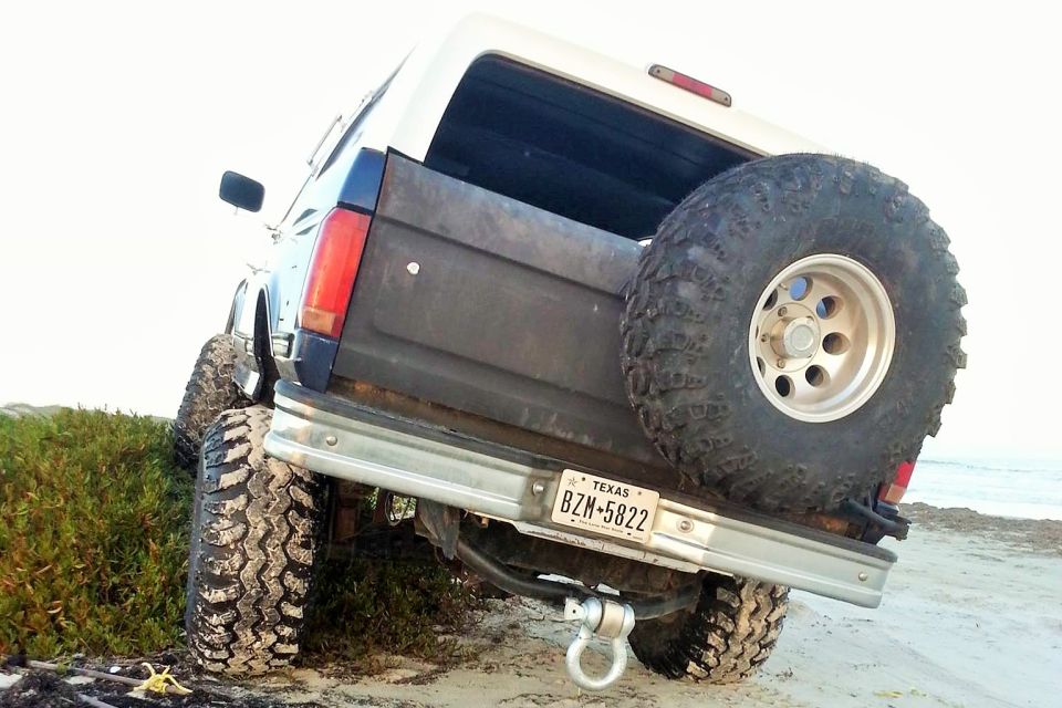 Lifted 1994 Ford Bronco on a beach, rear view, showing off-road tires and spare tire.