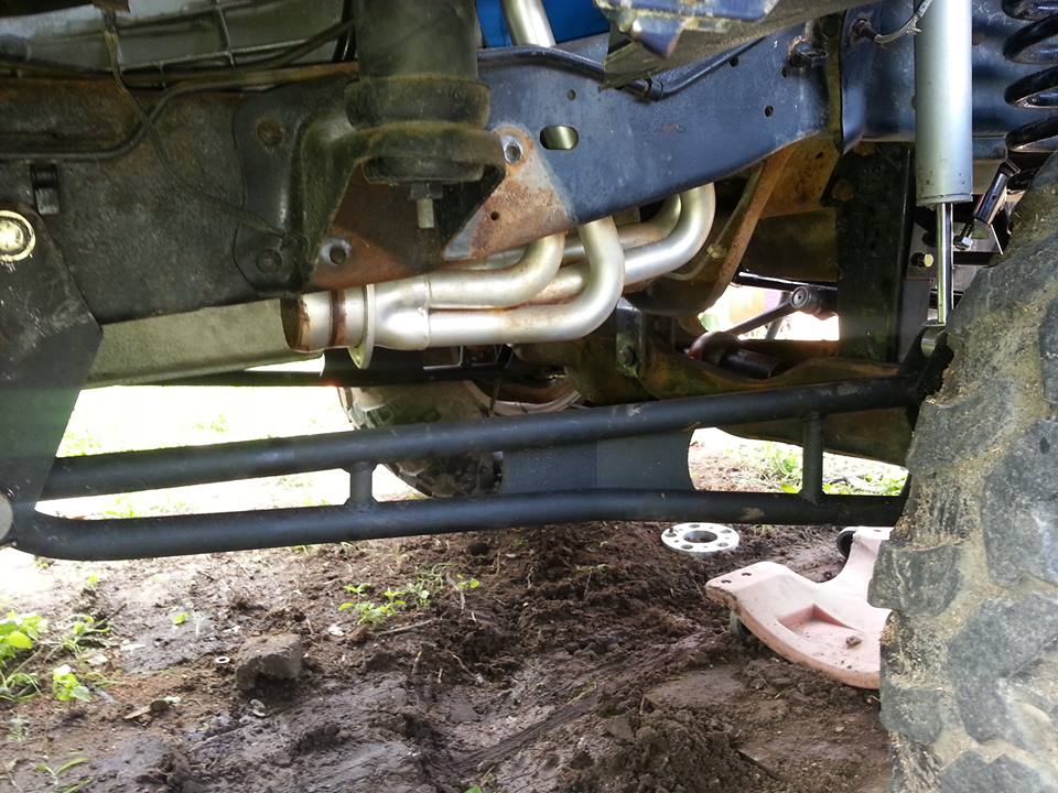Underside of a modified 4x4 vehicle showing exhaust header, suspension, and tire.