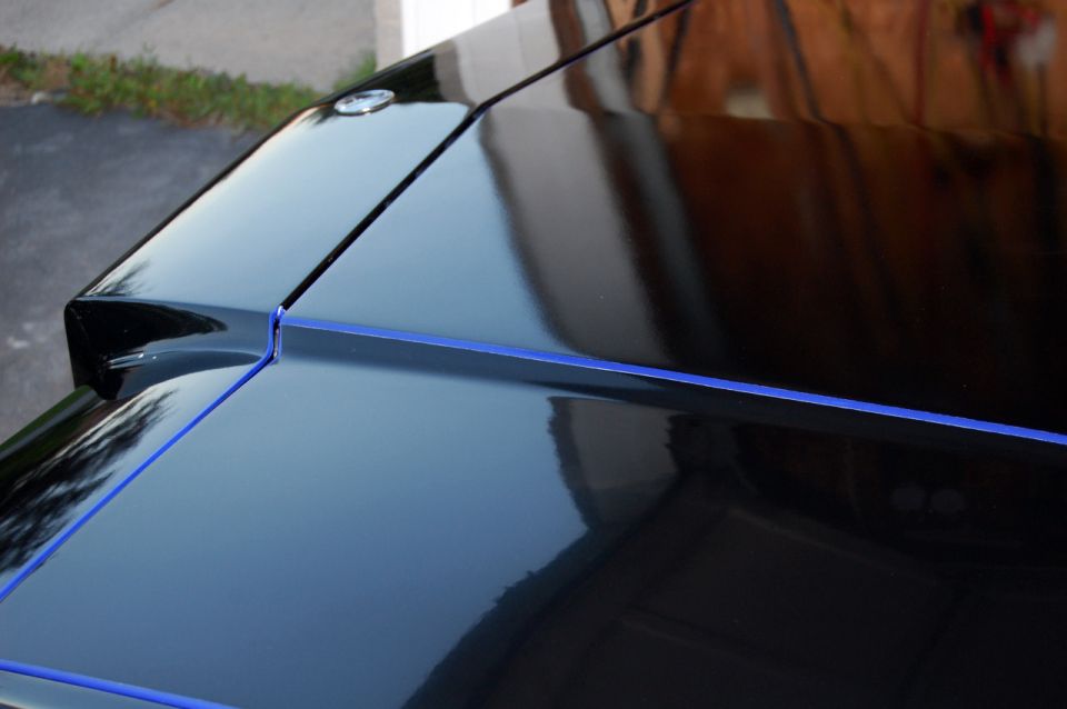 Glossy black car hood and trunk with blue pinstripe, showing reflections.