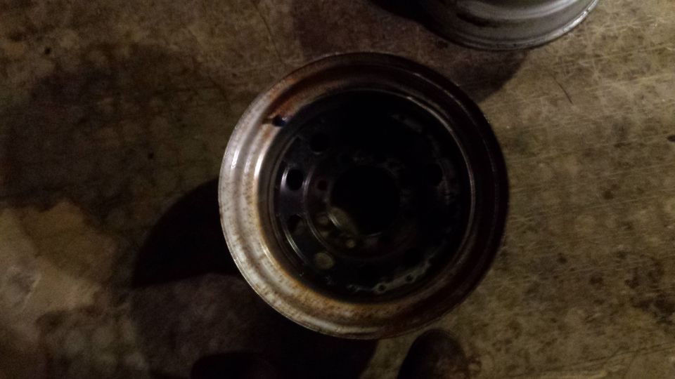 Rusty white steel wheel rim with lug nut holes on a concrete floor.