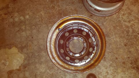 Rusty steel wheel rim with circular cutouts on concrete floor