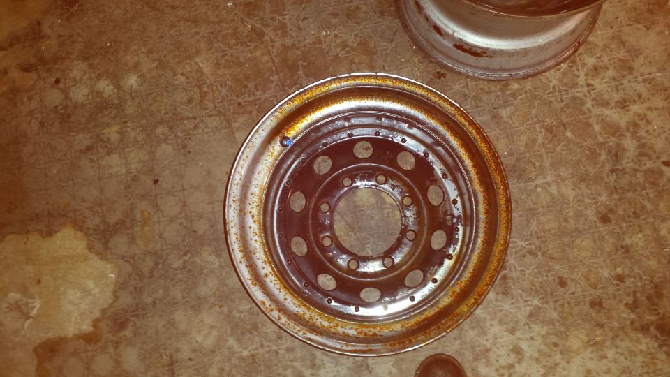 Rusty steel wheel rim with circular cutouts on concrete floor