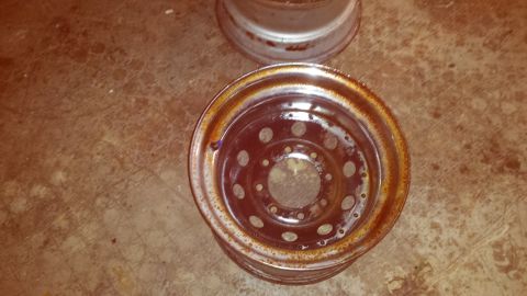 Two rusty steel wheels on a floor. One wheel is closer and shows bolt holes and a rusted rim.