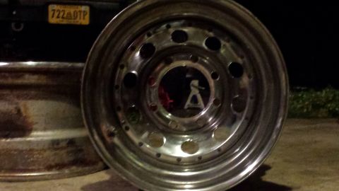 Shiny chrome wheel with lug nut holes, rusty wheel, and yellow license plate