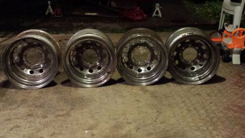 Four polished aluminum truck wheels with multiple holes, lined up on concrete.