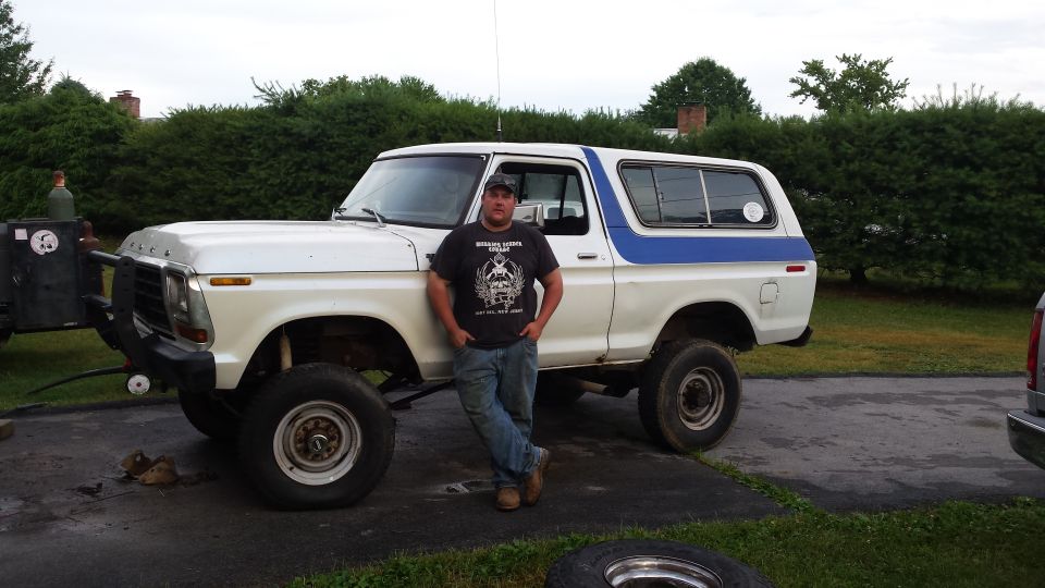 Man standing next to a lifted white and blue 1979 Ford Bronco.