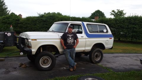 Man standing in front of a lifted white and blue 1979 Ford Bronco with a welding trailer.