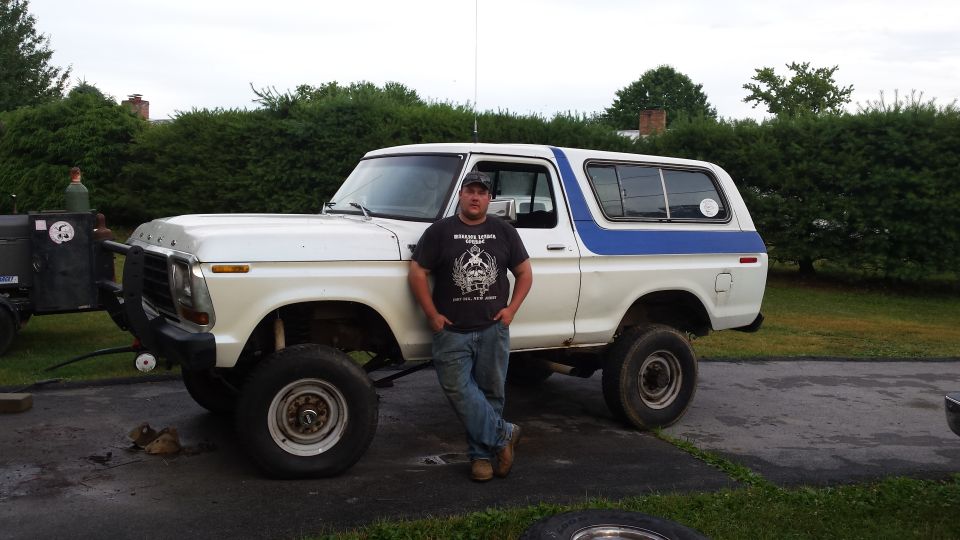 Man standing in front of a lifted white and blue 1979 Ford Bronco with a welding trailer.