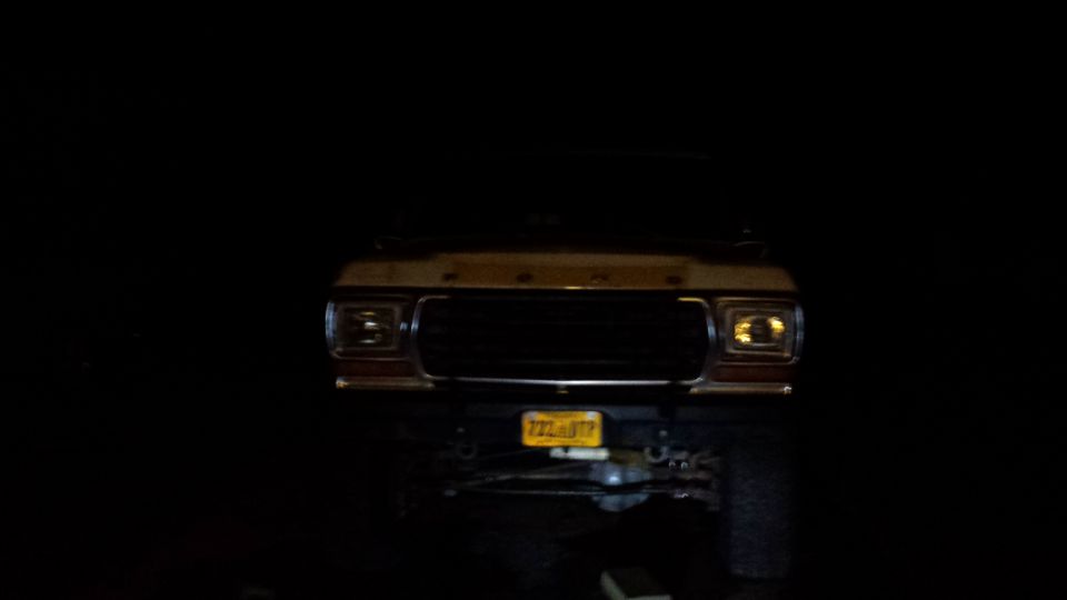 Front view of a vintage Ford Bronco at night, headlights on, yellow license plate visible.