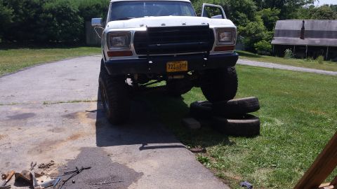 Lifted white 1979 Ford Bronco with black grille guard and stacked tires.