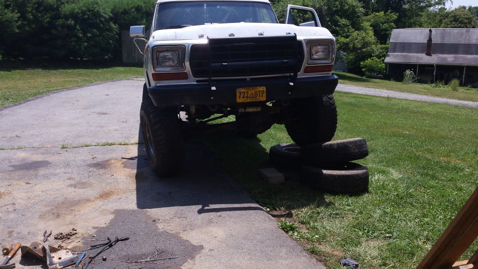 Lifted white 1979 Ford Bronco with black grille guard and stacked tires.