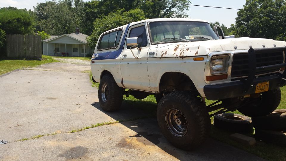 Lifted white and blue 1979 Ford Bronco with rust on a concrete driveway.