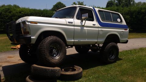 White 1979 Ford Bronco with blue stripe, front tire on old tires.