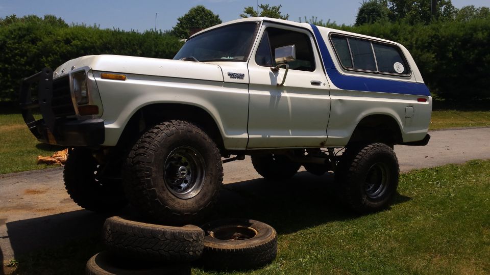 White 1979 Ford Bronco with blue stripe, front tire on old tires.
