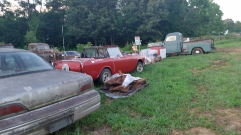 2015 Chevrolet new - A collection of vehicles and parts are parked in a grassy outdoor area. In the foreground, the rear of a weathered sedan is visible, with a…