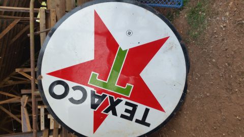2015 Chevrolet new - A round, vintage Texaco sign with a red star and green "T" logo is displayed outdoors, leaning against wooden structures. The sign shows we…