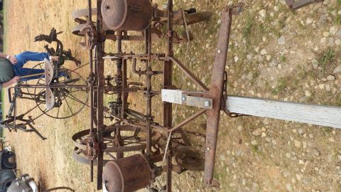 2015 Chevrolet new - An old, rusty farm implement with multiple wheels, gears, and hoppers is displayed outdoors on a gravelly dirt surface.
