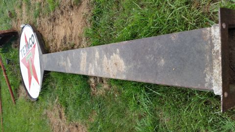 2015 Chevrolet new - A vintage Texaco sign with a red star and green 'T' is lying on its side in the grass. The sign is attached to a long, weathered metal pole.