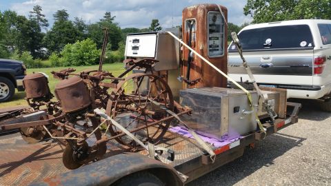2015 Chevrolet new - A rusty antique planter and a vintage gas pump are loaded onto a trailer, being towed by a white Ford F-150 pickup truck.