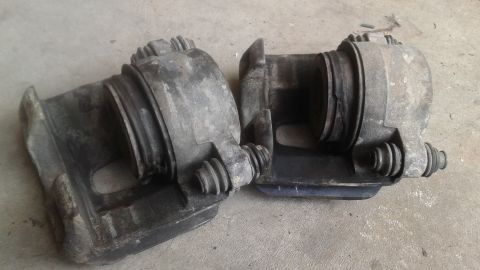 1996 Ford Bronco - Two used brake calipers are shown resting on a concrete surface. The calipers are gray and appear to be made of cast iron or aluminum.