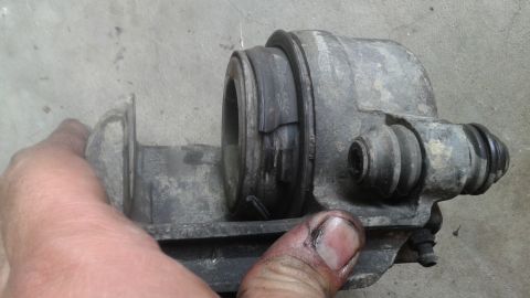 1996 Ford Bronco - A person's hand holds a dirty, gray brake caliper with a torn rubber dust boot. The caliper has a piston visible and appears to be a vehicl…