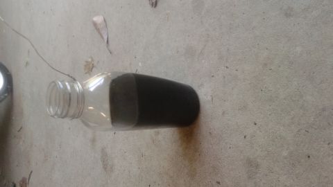 1996 Ford Bronco - A clear glass bottle lying on its side on a concrete surface. The bottle is partially filled with a dark, viscous liquid.