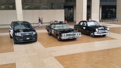1991 Ford LTD Crown Victoria - Photograph of three police vehicles parked outside a building at a car show, not a technical document.