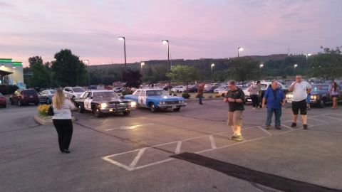 1991 Ford LTD Crown Victoria - Photo of vintage police cars and attendees at a car meet at dusk, not a technical document.