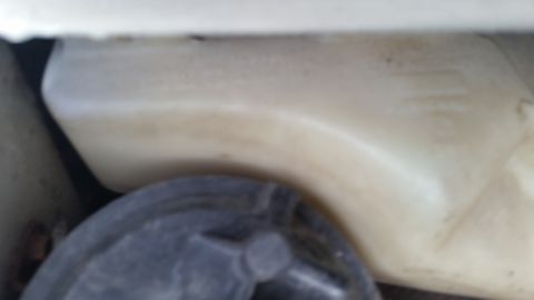 1991 Ford LTD Crown Victoria - Blurry photo of a plastic reservoir and rubber mount, not a technical document.