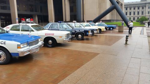 1991 Ford LTD Crown Victoria - Photo of a lineup of vintage police cars on a plaza, not a technical document.