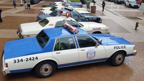 1991 Ford LTD Crown Victoria - Photo of vintage police cars lined up on a plaza, not a technical document.